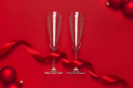 New Year Christmas Champagne glasses, Christmas balls, gold confetti stars on red background top view with copy space. Flat lay Xmas holiday 2020 celebration. Greeting card Festive decorations.の写真素材