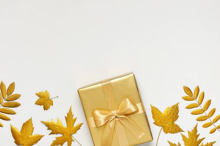 Flat lay Autumn holiday concept. Golden gift or present box with ribbon and golden autumn leaves on light gray background top view copy space. Surprise, congratulation, birthday, greeting card.の写真素材