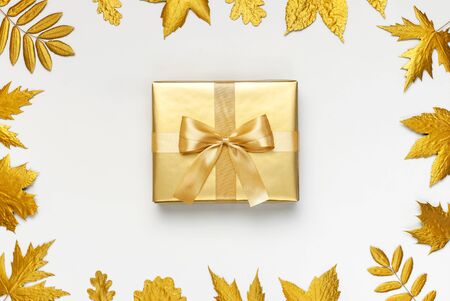 Flat lay Autumn holiday concept. Golden gift or present box with ribbon and golden autumn leaves on light gray background top view copy space. Surprise, congratulation, birthday, greeting card.の写真素材