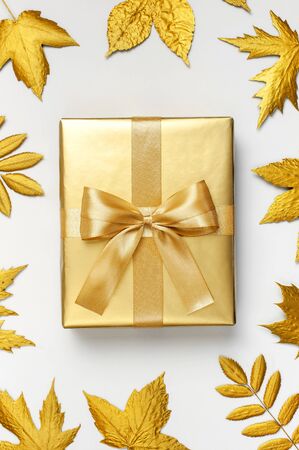 Flat lay Autumn holiday concept. Golden gift or present box with ribbon and golden autumn leaves on light gray background top view copy space. Surprise, congratulation, birthday, greeting card.の写真素材