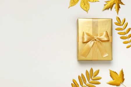Flat lay Autumn holiday concept. Golden gift or present box with ribbon and golden autumn leaves on light gray background top view copy space. Surprise, congratulation, birthday, greeting card.の写真素材