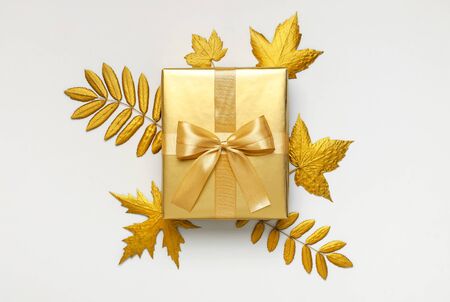 Flat lay Autumn holiday concept. Golden gift or present box with ribbon and golden autumn leaves on light gray background top view copy space. Surprise, congratulation, birthday, greeting card.の写真素材