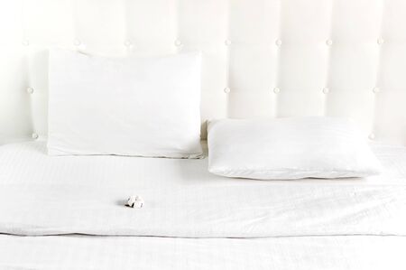 Soft white quilted pillow and cotton flower in bed on the background of white leather quilted headboard. Clean pillow, part of bed close-up, comfort. Quilted headboard background, bedding mockup.の写真素材