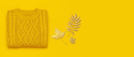 Autumn flat lay composition. Orange yellow knitted woolen female sweater and golden leaves on yellow background top view. Fashionable women's fall accessories. Cozy Knit Jumper Stylish Lady Clothes.の写真素材