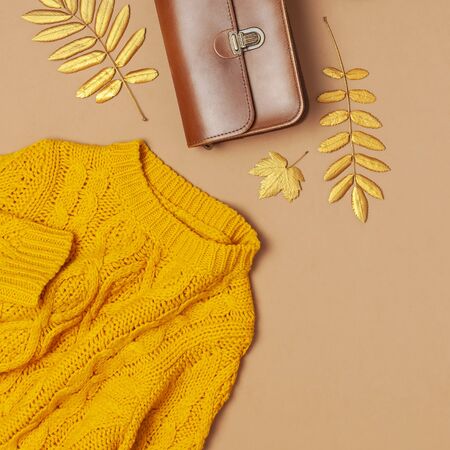 Brown leather women bag, orange knitted sweater, golden autumn leaf on brown background top view flat lay copy space. Fashionable women's accessories. Autumn Fashion Concept. Stylish Lady Clothes.の写真素材