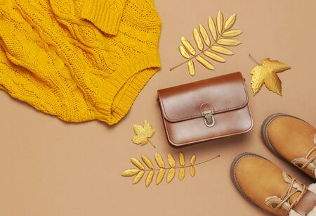 Brown leather women bag, orange knitted sweater, warm boots, golden autumn leaf on brown background top view flat lay. Fashionable women's accessories. Autumn Fashion Concept. Stylish Lady Clothes.の写真素材