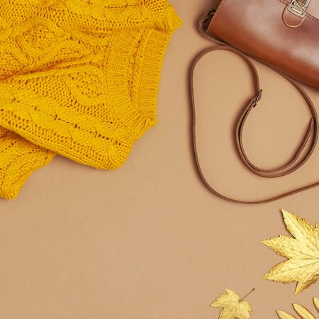 Brown leather women bag, orange knitted sweater, golden autumn leaf on brown background top view flat lay copy space. Fashionable women's accessories. Autumn Fashion Concept. Stylish Lady Clothes.の写真素材