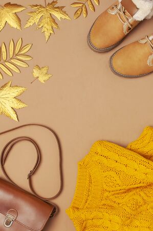 Brown leather women bag, orange knitted sweater, warm boots, golden autumn leaf on brown background top view flat lay. Fashionable women's accessories. Autumn Fashion Concept. Stylish Lady Clothes.の写真素材