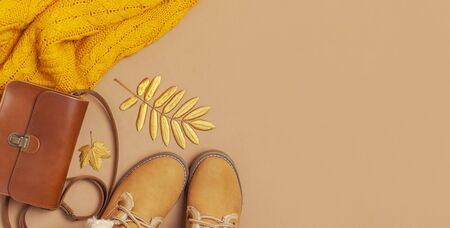 Brown leather women bag, orange knitted sweater, warm boots, golden autumn leaf on brown background top view flat lay. Fashionable women's accessories. Autumn Fashion Concept. Stylish Lady Clothes.の写真素材