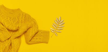 Autumn flat lay composition. Orange yellow knitted woolen female sweater and golden leaves on yellow background top view. Fashionable women's fall accessories. Cozy Knit Jumper Stylish Lady Clothes.の写真素材