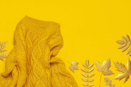Autumn flat lay composition. Orange yellow knitted woolen female sweater and golden leaves on yellow background top view. Fashionable women's fall accessories. Cozy Knit Jumper Stylish Lady Clothes.の写真素材