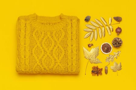 Autumn flat lay composition. Orange yellow knitted woolen female sweater and golden leaves on yellow background top view. Fashionable women's fall accessories. Cozy Knit Jumper Stylish Lady Clothes.の写真素材