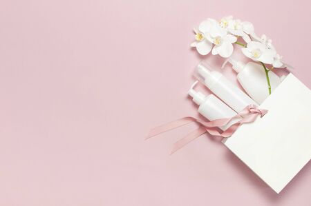 Flat lay White cosmetic bottle containers gift bag White Phalaenopsis orchid flowers on pink background top view. Cosmetics SPA branding mock-up Natural organic beauty product concept Minimalism style.の写真素材