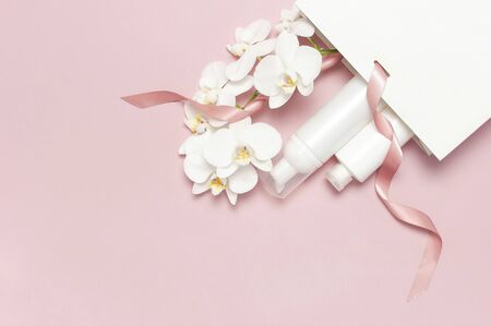 Flat lay White cosmetic bottle containers gift bag White Phalaenopsis orchid flowers on pink background top view. Cosmetics SPA branding mock-up Natural organic beauty product concept Minimalism style.の写真素材