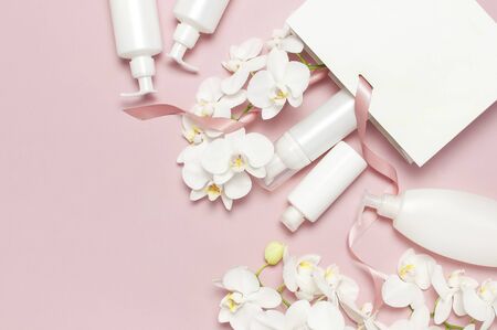 Flat lay White cosmetic bottle containers gift bag White Phalaenopsis orchid flowers on pink background top view. Cosmetics SPA branding mock-up Natural organic beauty product concept Minimalism style.の写真素材