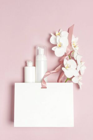 Flat lay White cosmetic bottle containers gift bag White Phalaenopsis orchid flowers on pink background top view. Cosmetics SPA branding mock-up Natural organic beauty product concept Minimalism style.の写真素材