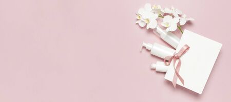 Flat lay White cosmetic bottle containers gift bag White Phalaenopsis orchid flowers on pink background top view. Cosmetics SPA branding mock-up Natural organic beauty product concept Minimalism style.の写真素材