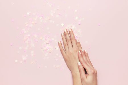 Stylish fashionable female manicure in pastel colors. Hands of young girl on pink background with festive confetti. Minimalist manicure trend. Flat lay, top view, copy space for your text.の写真素材