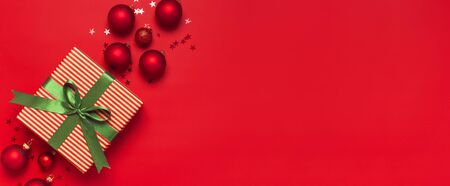 Christmas background. Gift with green ribbon, red Christmas balls, confetti shape of stars on red background top view. New Year presents Festive decorations Flat lay Xmas holiday 2020 celebration.の写真素材