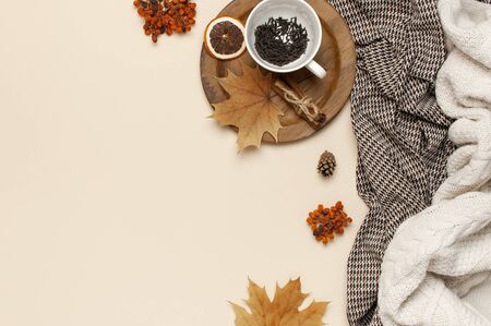 Flat lay autumn composition. White cup with tea leaves, wooden plate, knitted fashion sweater or plaid, pants in a pattern, yellow maple leaves, cinnamon, orange on beige background top view copy space.の写真素材