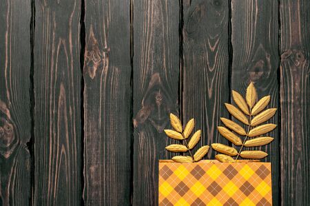 Flat lay creative autumn composition. Gift orange bag in cage and Golden leaves on dark wooden background top view copy space. Fall concept. Autumn background. Minimal concept idea, floral design.の写真素材