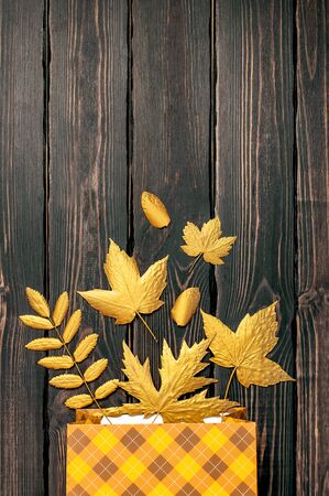 Flat lay creative autumn composition. Gift orange bag in cage and Golden leaves on dark wooden background top view copy space. Fall concept. Autumn background. Minimal concept idea, floral design.の写真素材
