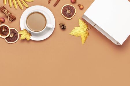 Autumn composition. White cup of coffee or cocoa, golden maple leaves, cinnamon, dried orange, pine cone, pomegranate on beige background. Flat lay, top view, copy space. Autumn, fall concept.の写真素材