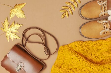 Brown leather women bag, orange knitted sweater, warm boots, golden autumn leaf on brown background top view flat lay. Fashionable womens accessories. Autumn Fashion Concept. Stylish Lady Clothes.の写真素材
