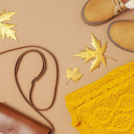 Brown leather women bag, orange knitted sweater, warm boots, golden autumn leaf on brown background top view flat lay. Fashionable womens accessories. Autumn Fashion Concept. Stylish Lady Clothes.の写真素材