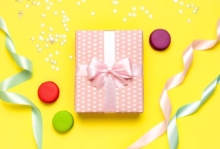 Gift or present box, beautiful festive ribbon, macaroon, confetti on yellow background top view. Flat lay composition for celebration, birthday, Valentine's Day, March 8, mother day.の写真素材