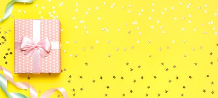 Gift or present box, beautiful festive ribbon, confetti on yellow background top view. Flat lay composition for celebration, birthday, Valentine's Day, March 8, mother day, wedding. Congratulation.の写真素材