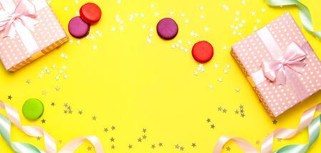 Gift or present box, beautiful festive ribbon, macaroon, confetti on yellow background top view. Flat lay composition for celebration, birthday, Valentine's Day, March 8, mother day.の写真素材
