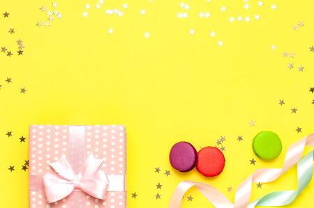 Gift or present box, beautiful festive ribbon, macaroon, confetti on yellow background top view. Flat lay composition for celebration, birthday, Valentine's Day, March 8, mother day.の写真素材