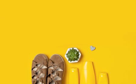 Yellow bottles of sunscreen cream, women's sandals, green succulent on bright yellow background top view flat lay copy space. Sun protection. Summer background, vacation, travel concept.の写真素材