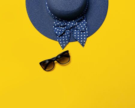 Women s summer blue straw hat and sunglasses on yellow background top view flat lay copy space. Summer travel vacation concept, single item. Female accessory, summer background.の写真素材