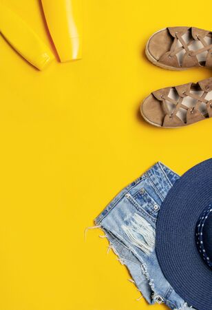 Female summer fashion background. Clothes and accessories on yellow background. Blue hat, denim shorts, sandals, sunglasses, sunscreen, phone. Flat lay top view, beauty or fashion blog concept.の写真素材