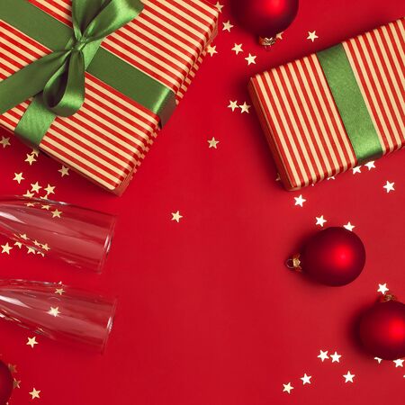 New Year Christmas presents, Christmas balls, champagne glasses, gold confetti stars on red background top view. Flat lay Xmas holiday 2020 celebration. Gift boxes greeting card Festive decorations.の写真素材