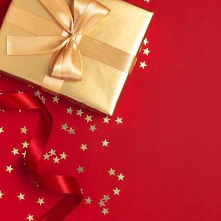 New Year Christmas golden presents with ribbon, Christmas balls, gold confetti stars on red background top view. Flat lay Xmas holiday 2020 celebration. Gift boxes greeting card Festive decorations.の写真素材