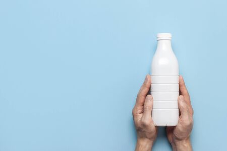 White plastic bottle containers for dairy products in male hands on blue background top view flat lay. Plastic Kefir Yogurt Milk Bottle. Packaging template mockup. Layout for your design.の写真素材