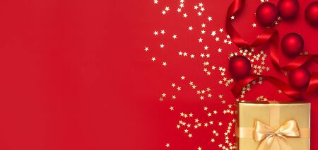 New Year Christmas golden presents with ribbon, Christmas balls, gold confetti stars on red background top view. Flat lay Xmas holiday 2020 celebration. Gift boxes greeting card Festive decorations.の写真素材