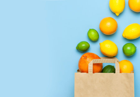 Creative background with tropical fruits. Orange, lemon, lime, grapefruit drop out of paper bag on blue background. Flat lay top view copy space. Food concept, vitamin C, disease prevention, flu.の写真素材