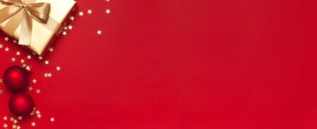 Flat lay Xmas holiday 2020 celebration. New Year Christmas golden presents with ribbon, Christmas balls, gold confetti stars on red background top view. Gift boxes greeting card Festive decorations.の写真素材