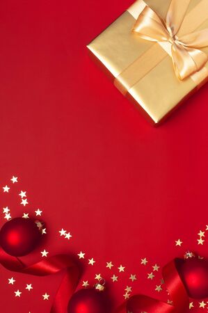 Flat lay Xmas holiday 2020 celebration. New Year Christmas golden presents with ribbon, Christmas balls, gold confetti stars on red background top view. Gift boxes greeting card Festive decorations.の写真素材