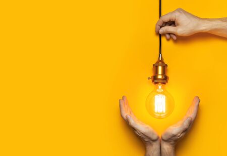 Vintage fashionable edison lamp in male hands on bright yellow background. Top view flat lay copy space. Creative idea concept, designer lamp, modern interior item. Lighting, electricity.の写真素材