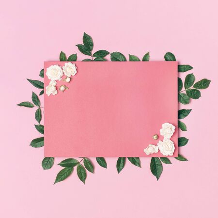 Flowers composition. Pink blank paper, white fresh roses and green leaves on gentle pink background. Flat lay, top view, copy space. Flower card, greeting, holiday mockup. Valentine's Day background.の写真素材