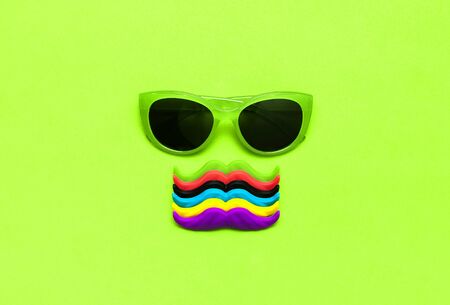 Creative party decoration concept. Multi-colored mustache Sunglasses props for photo booths carnival parties on green background top view flat lay copy space. Father's day Men's health awareness month.の写真素材