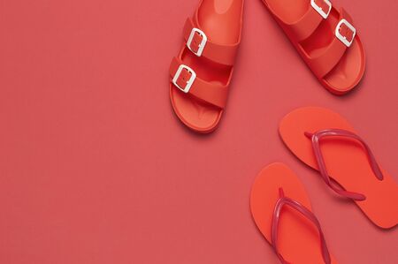 Fashionable beach coral flip flops and sandals on bright coral background. Flat lay, top view, copy space. Creative beach concept, stylish summer shoes, vacation, travel. Trend coral color.の写真素材
