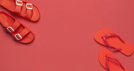 Fashionable beach coral flip flops and sandals on bright coral background. Flat lay, top view, copy space. Creative beach concept, stylish summer shoes, vacation, travel. Trend coral color.の写真素材