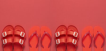 Fashionable beach coral flip flops and sandals on bright coral background. Flat lay, top view, copy space. Creative beach concept, stylish summer shoes, vacation, travel. Trend coral color.の写真素材