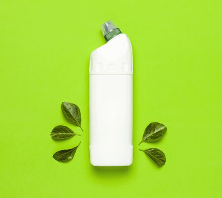 White plastic bottle for liquid detergent, cleaning agent, bleach, antibacterial gel with natural plant extract and green leaves on green background. Eco style cleaning concept. Flat lay top view.の写真素材